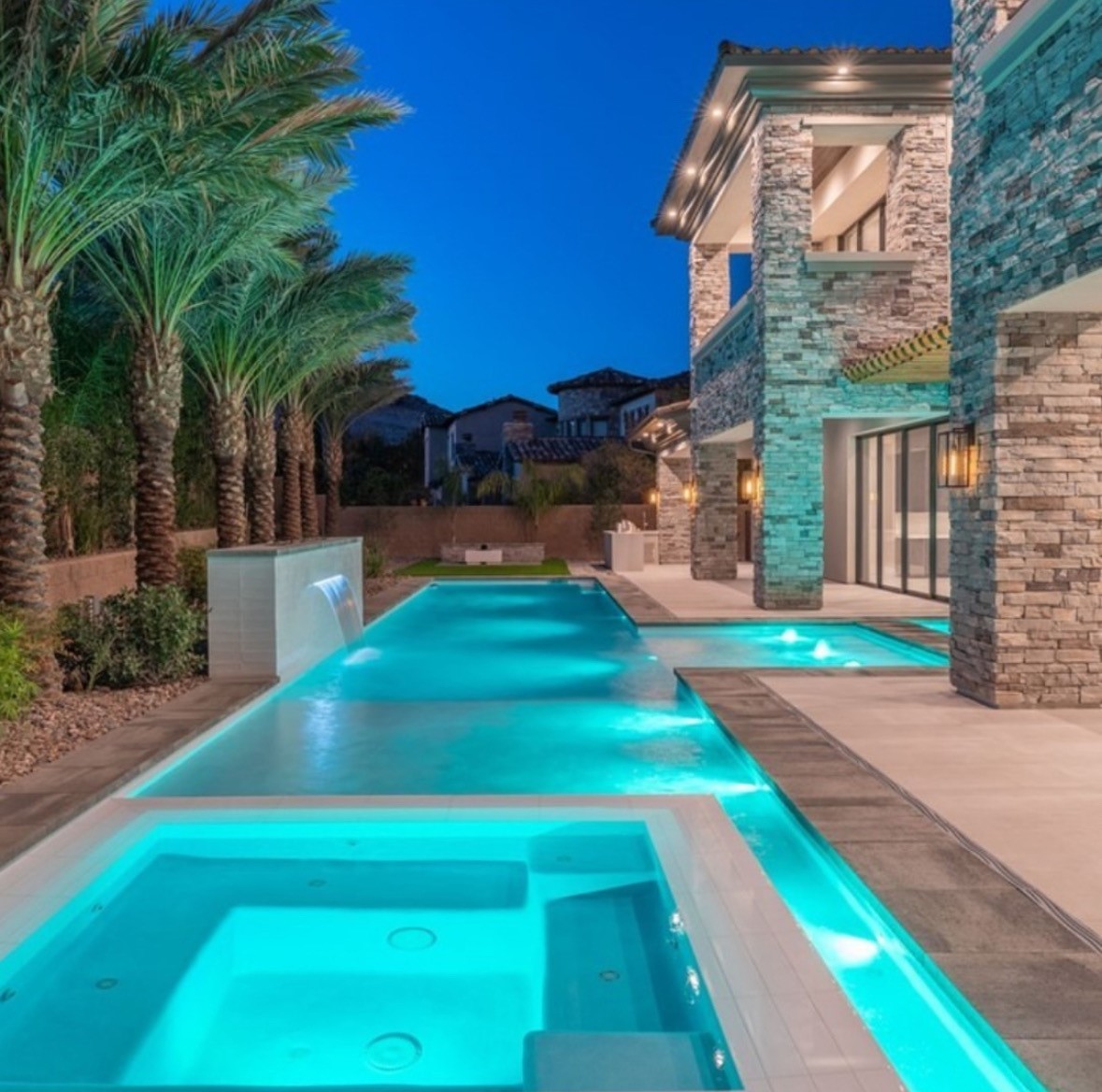 Backyard of a Las Vegas luxury home with a lit turquoise pool and spa at dusk